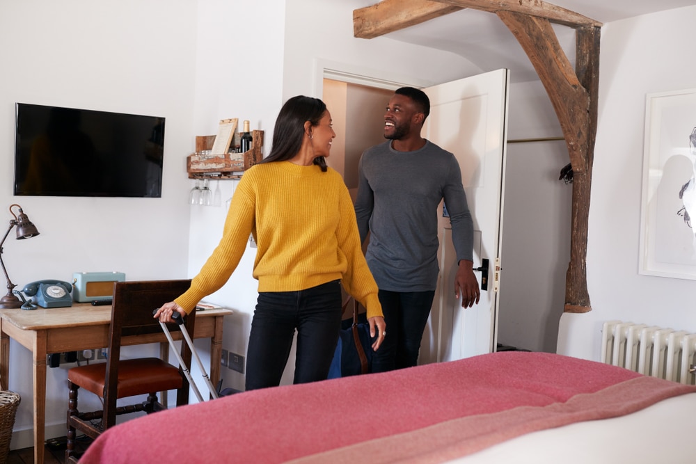 Smiling couple embracing in bedroom, woman in yellow sweater and man in gray shirt