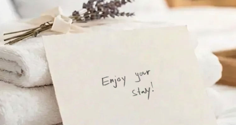 Folded white towels topped with a sprig of dried lavender and a handwritten card that reads "Enjoy your stay!"